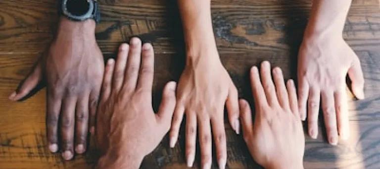 a picture showing palm down hands on the table from different minority background people