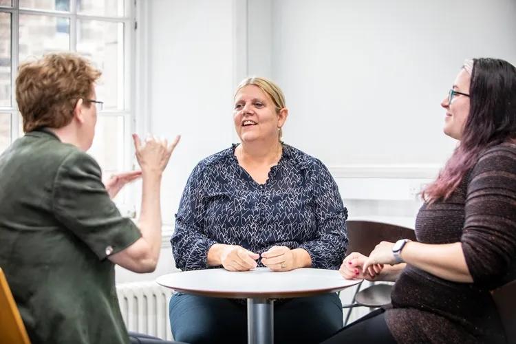 Three women sat around a table doing BSL