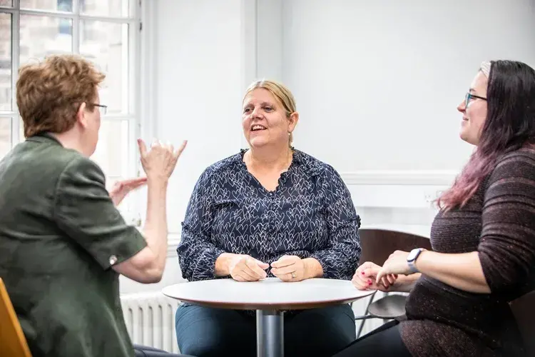 Three women sat around a table doing BSL
